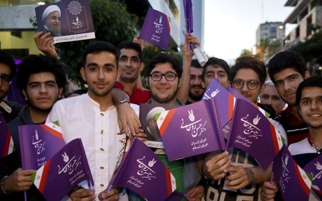 In this May 10, 2017 photo, supporters of Iranian President Hassan Rouhani hold his posters for May 19 presidential election in downtown Tehran, Iran. (AP Photo/Ebrahim Noroozi)