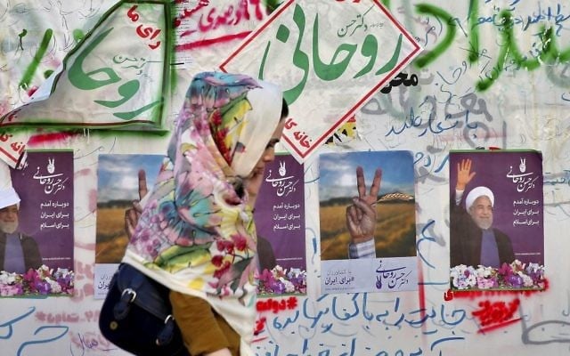 In this Wednesday, May 10, 2017 photo, an Iranian woman walks past electoral posters and hand written slogans for presidential election candidates in downtown Tehran, Iran. (AP Photo/Ebrahim Noroozi) 