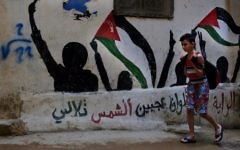 In this Thursday, May 4, 2017 photo, a boy walks by graffiti of Palestinian flags with Arabic reading: "The flag is four colors that shine on the face of the sun" in the Bourj al-Barajneh Palestinian refugee camp in Beirut, Lebanon. (AP Photo/Bilal Hussein)