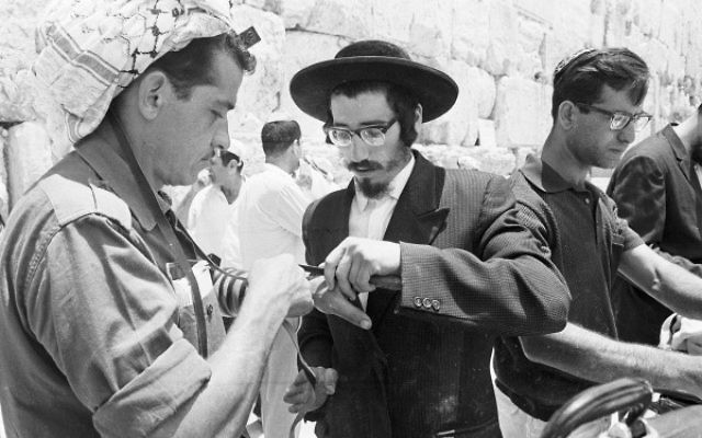 An ultra-orthodox man helps a soldier to lay Tefillin at the Western Wall, June 22, 1967. (From the collection of Dan Hadani, National Library of Israel). An ultra-orthodox man helps a soldier to lay Tefillin at the Western Wall, June 22, 1967. (From the collection of Dan Hadani, National Library of Israel).