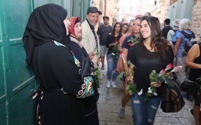 During a peace walk organized by Tag Meir a woman hands flowers to Arab shopkeepers in Jerusalem's Old City ahead of the Jerusalem Day flag parade, May 24, 2017. (Courtesy)