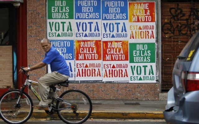 A man rides his bicycle in front of a wall covered with campaign posters promoting Puerto Rico’s statehood in San Juan, on June 9, 2017. (Ricardo Arduengo/AFP) A man rides his bicycle in front of a wall covered with campaign posters promoting Puerto Rico’s statehood in San Juan, on June 9, 2017. (Ricardo Arduengo/AFP)