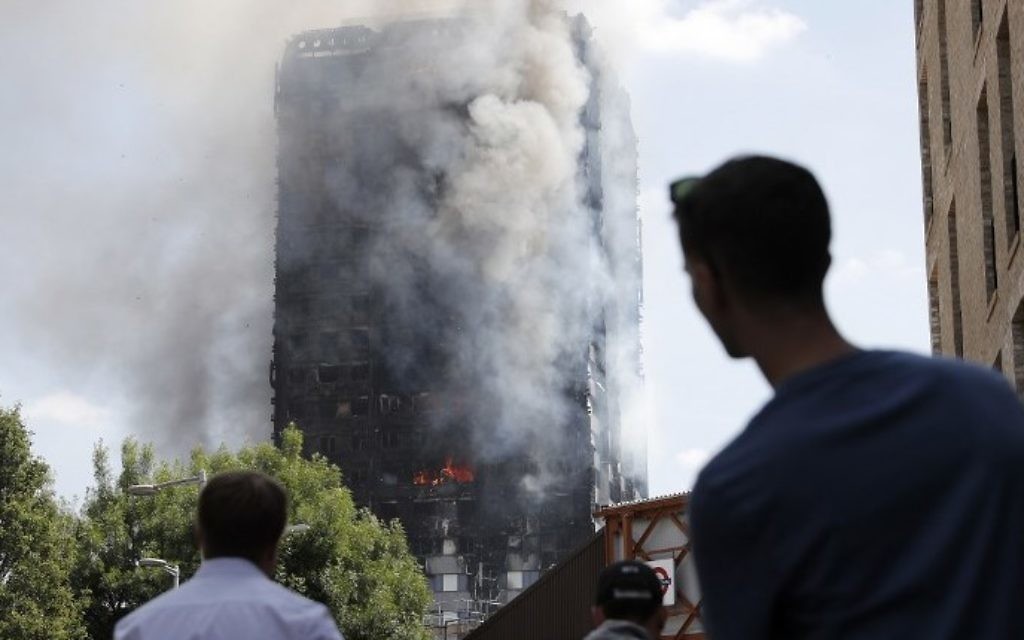 Pedestrians look up towards Grenfell Tower, a residential block of flats in west London on June 14, 2017, as firefighters continue to control a fire that engulfed the building in the early hours of the morning. (AFP PHOTO / Adrian DENNIS)
