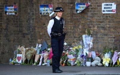 A police officer stands on duty near tributes and flowers at a police cordon in the Finsbury Park area of north London on June 19, 2017. (AFP/ Isabel INFANTES)