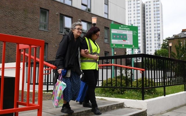 A resident (L) is helped by a council official as she leaves Burnham Tower residential block on the Chalcots Estate in north London on June 24, 2017 as residents evacuate because of fire safety concerns. (AFP PHOTO / Justin TALLIS)