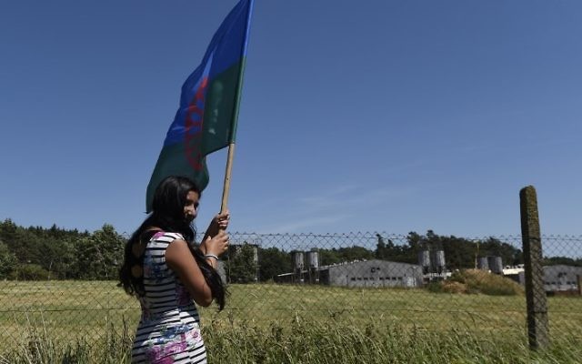 A Roma girl holds a flag as she stands in front of the fence of the industrial pig farm situated at the site of a former concentration camp in Lety, Czech Republic, on June 24, 2017, during the "Dignity for Lety" commemorational event organized by the European Grassroots Antiracist Movement (EGAM). (Michal Cizek/AFP) A Roma girl holds a flag as she stands in front of the fence of the industrial pig farm situated at the site of a former concentration camp in Lety, Czech Republic, on June 24, 2017, during the "Dignity for Lety" commemorational event organized by the European Grassroots Antiracist Movement (EGAM). (Michal Cizek/AFP)