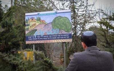 A man looks at a sign for the 50th anniversary celebrations of Kfar Etzion at the entrance to Kfar Etzion, in the West Bank on January 30, 2017. (Gershon Elinson/Flash90)