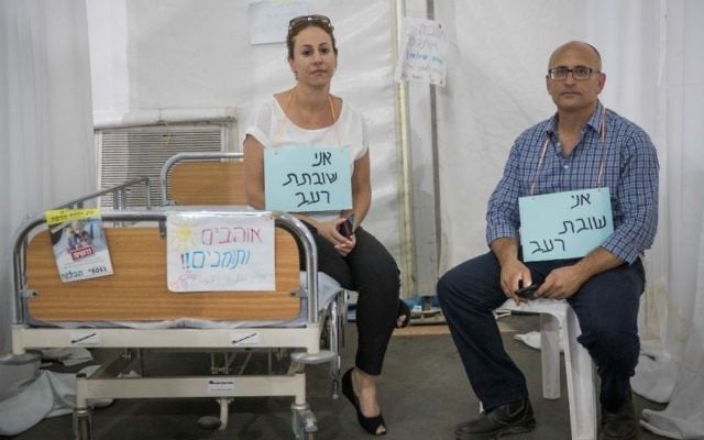 Shlomo Ben Dor (R) and Pazit Ben Israel sit at the protest tent of the Hadassah Hospital hemato-ontology department in Sacher Park, Jerusalem, wearing signs which say 'I'm on hunger strike,' June 25, 2017 (Yonatan Sindel/Flash90) Shlomo Ben Dor (R) and Pazit Ben Israel sit at the protest tent of the Hadassah Hospital hemato-ontology department in Sacher Park, Jerusalem, wearing signs which say 'I'm on hunger strike,' June 25, 2017 (Yonatan Sindel/Flash90)