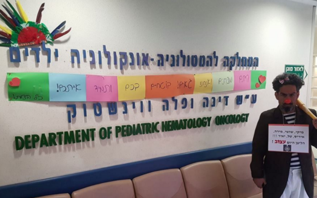 A medical clown at Hadassah's pediatric hematology-oncology department in March, shortly after six doctors resigned. 'Today the clown is sad,' reads his sign (Screenshot Facebook) A medical clown at Hadassah's pediatric hematology-oncology department in March, shortly after six doctors resigned. 'Today the clown is sad,' reads his sign (Screenshot Facebook)