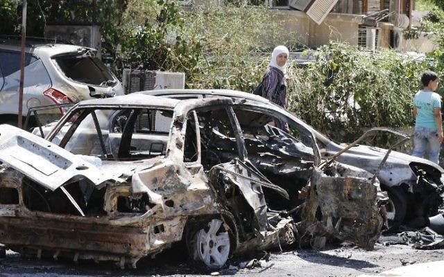 Syrians walk past a charred vehicle at the site of a suicide bombing in Damascus on July 2, 2017. (AFP Photo/Louai Beshara) Syrians walk past a charred vehicle at the site of a suicide bombing in Damascus on July 2, 2017. (AFP Photo/Louai Beshara)