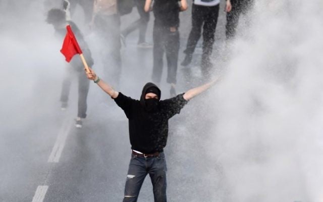 Police use water cannons towards a protester with a red flag during the "Welcome to Hell" rally against the G20 summit in Hamburg, Germany, on July 6, 2017. (AFP Photo/John Macdougall)