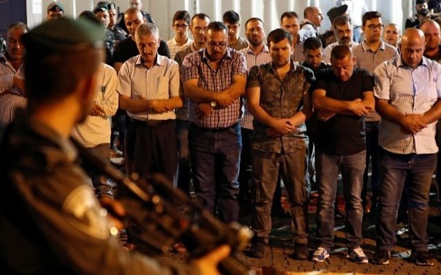 Israeli security forces stand guard in front of Palestinian Muslim worshipers praying outside Lions Gate, a main entrance to the Al-Aqsa Mosque compound in Jerusalem's Old City, on July 19, 2017, as the latter protest against new Israeli security measures implemented at the holy site (AFP PHOTO / Ahmad GHARABLI