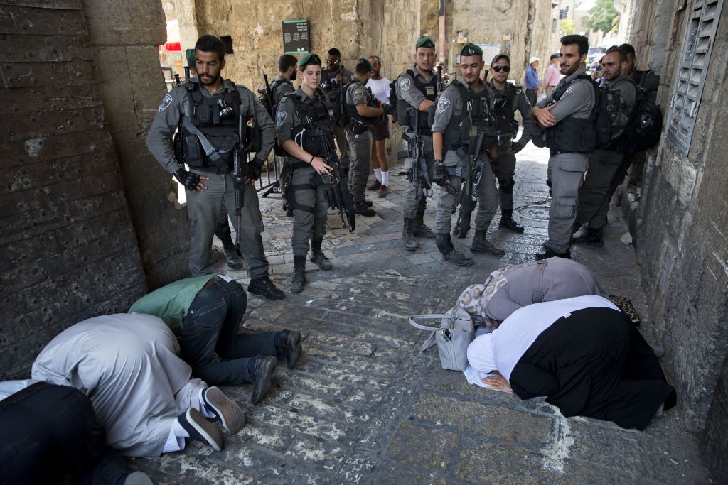 Palestinians pray as Israeli border police officers stand guard at the Lions' Gate in Jerusalem's Old City, Tuesday, July 25, 2017. (AP Photo/Oded Balilty) Palestinians pray as Israeli border police officers stand guard at the Lions' Gate in Jerusalem's Old City, Tuesday, July 25, 2017. (AP Photo/Oded Balilty)