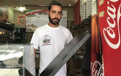 Shlomi Madar holds up the counter-top that separated him from the Palestinian terrorist who tried to stab him in his pizza kiosk in Petah Tikva, July 24, 2017. (Jacob Magid/Times of Israel)