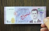 In this photo released by the Syrian official news agency SANA, a man displays a new bank note of 2,000 Syrian Lira, ($3.9) featuring the face of President Bashar Assad, during a press conference for Central Bank Governor Duraid Durgham in Damascus, Syria, July 2, 2017. (SANA via AP)