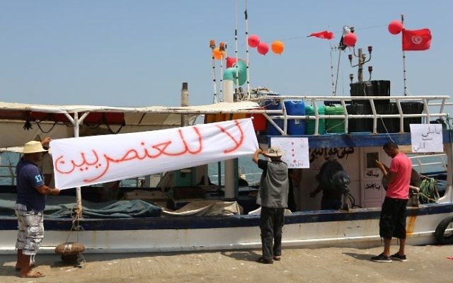 Tunisian fishermen hang banners as they gather on August 6, 2017 in the port of Zarzis in southeastern Tunisia to protest against a possible berthing of the C-Star vessel, hired by far-right activists from a group which calls itself 'Generation Identity' to prevent would-be migrants from reaching Europe. The writing in Arabic reads: 'No to Racism' (AFP PHOTO / FATHI NASRI) Tunisian fishermen hang banners as they gather on August 6, 2017 in the port of Zarzis in southeastern Tunisia to protest against a possible berthing of the C-Star vessel, hired by far-right activists from a group which calls itself 'Generation Identity' to prevent would-be migrants from reaching Europe. The writing in Arabic reads: 'No to Racism' (AFP PHOTO / FATHI NASRI)