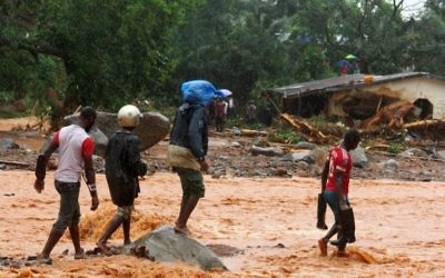 Residents walk through floodwaters past a damaged building in an area of Freetown on August 14, 2017, after landslides struck the capital of the west African state of Sierra Leone. (AFP PHOTO / SAIDU BAH)