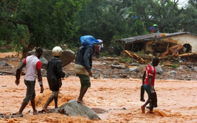Residents walk through floodwaters past a damaged building in an area of Freetown on August 14, 2017, after landslides struck the capital of the west African state of Sierra Leone. (AFP PHOTO / SAIDU BAH) Residents walk through floodwaters past a damaged building in an area of Freetown on August 14, 2017, after landslides struck the capital of the west African state of Sierra Leone. (AFP PHOTO / SAIDU BAH)