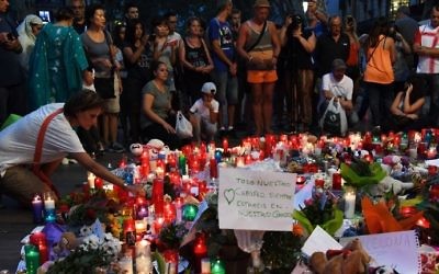 People stand next to flowers, candles and other items set up on the Las Ramblas boulevard in Barcelona as they pay tribute to the victims of the Barcelona attack, a day after a van plowed into the crowd, killing 14 and injuring over 100 on August 18, 2017. (AFP PHOTO / PASCAL GUYOT)