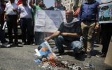 A picture taken on August 24, 2017 in the West Bank city of Ramallah shows a Palestinian holding a burnt flyer depicting US President Donald J. Trump defaced with cartoon shoes on his head, during a protest against the arrival of a US delegation headed by senior White House advisor Jared Kushner. (AFP/Abbas Momani)