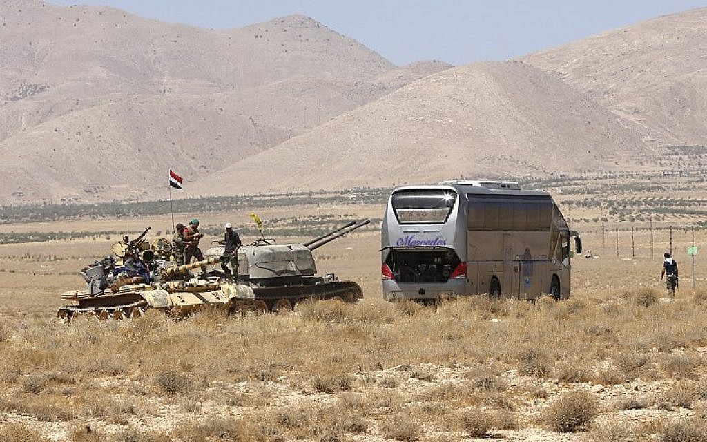 Syrian forces members stand on a tank next to a vehicle waiting to transport Islamic State group members in the Qara area in Syria's Qalamoun region on August 28, 2017. (AFP/Louai Beshara)