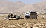 Syrian forces members stand on a tank next to a vehicle waiting to transport Islamic State group members in the Qara area in Syria's Qalamoun region on August 28, 2017. (AFP/Louai Beshara)