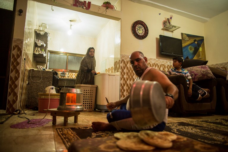 This photo taken on July 12, 2017 shows a Palestinian man preparing bread as his wife washes clothes during the few hours of electricity they receive every day, at the al-Shati refugee camp in Gaza City. (AFP PHOTO / MAHMUD HAMS)