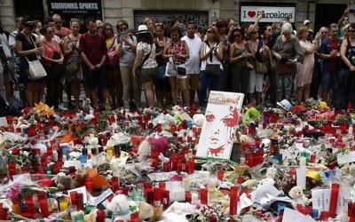 People stand next to candles and flowers placed on the ground after a terror attack that killed 14 people and wounded over 120 in Barcelona, Spain, Sunday, Aug. 20, 2017. (AP Photo/Manu Fernandez)