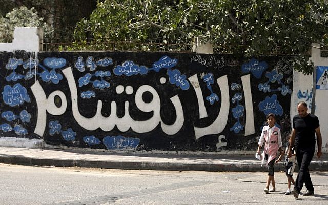 A Palestinian man and his daughter walk past a graffiti reading in Arabic 'Division' in Gaza City, on September 17, 2017, after Hamas announced it had agreed to steps toward resolving a decade-long split with the Fatah movement and was ready to hold elections. (AFP/Mahmud Hams) A Palestinian man and his daughter walk past a graffiti reading in Arabic 'Division' in Gaza City, on September 17, 2017, after Hamas announced it had agreed to steps toward resolving a decade-long split with the Fatah movement and was ready to hold elections. (AFP/Mahmud Hams)