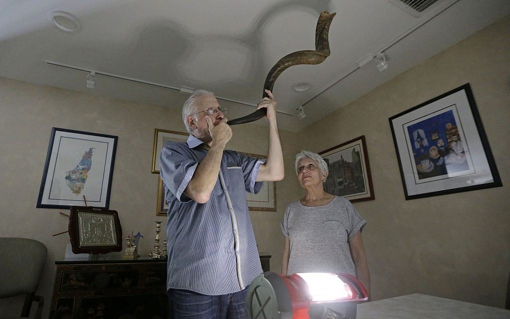 Michael Andron blows the shofar as he prepares for Rosh Hashanah, as his wife Lillian watches as they use a battery powered lantern to illuminate the room at their home, Tuesday, Sept.19, 2017, in Miami. (AP/Alan Diaz) Michael Andron blows the shofar as he prepares for Rosh Hashanah, as his wife Lillian watches as they use a battery powered lantern to illuminate the room at their home, Tuesday, Sept.19, 2017, in Miami. (AP/Alan Diaz)