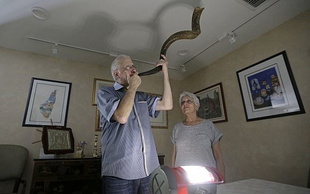Michael Andron blows the shofar as he prepares for Rosh Hashanah, as his wife Lillian watches as they use a battery powered lantern to illuminate the room at their home, Tuesday, Sept.19, 2017, in Miami. (AP/Alan Diaz)