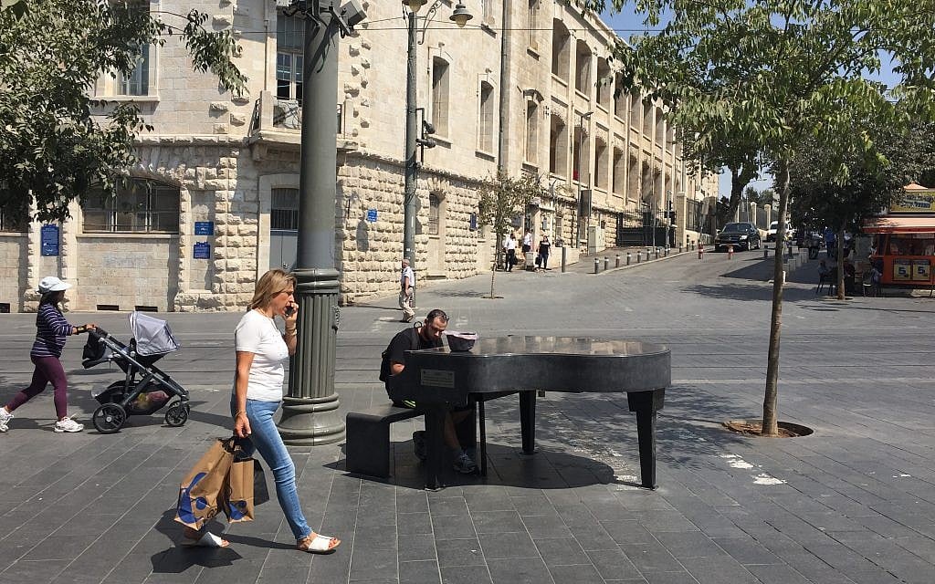 Passersby and a pianist at the Cadenza Piano temporarily installed at a busy crossroads in downtown Jerusalem, bringing music to the public (Jessica Steinberg/Times of Israel) Passersby and a pianist at the Cadenza Piano temporarily installed at a busy crossroads in downtown Jerusalem, bringing music to the public (Jessica Steinberg/Times of Israel)