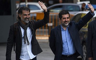Catalan National Assembly (ANC) president Jordi Sanchez (C), and Pro-independence Catalan Omnium cultural language association president Jordi Cuixart (L), who are under investigation for sedition, wave as they arrive at the High Court in Madrid on October 16, 2017.  / AFP PHOTO/GABRIEL BOUYS)