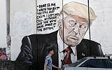 A man walks past a new piece of graffiti depicting US President Donald Trump on the Israeli separation barrier separating the West Bank town of Bethlehem from Jerusalem on October 15, 2017. (AFP Photo/Thomas Coex)