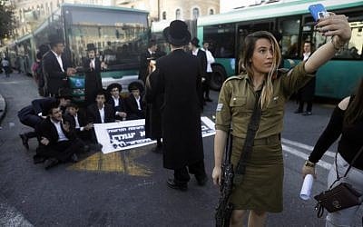 A female IDF soldier uses her cell phone to take a selfie as ultra-Orthodox Jews take part in a demonstration in Jerusalem against the conscription of members of the ultra-Orthodox community to the IDF on October 19, 2017. (AFP Photo/Menahem Kahana)