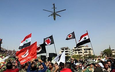 Syrians wave their national flags and those of the Syrian Social Nationalist Party in a stadium as a Russian-made Mil Mi-24 helicopter gunship hovers above during the funeral for Brigadier General Issam Zahreddine, in the southern city of Suwaida on October 20, 2017. (AFP/Stringer)
