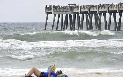 A beachgoer relaxes on the beach on Saturday October 7, 2017, as Hurricane Nate pushes waves from the Gulf of Mexico against the fishing pier in Navarre Beach, Florida (Nick Tomecek/Northwest Florida Daily News via AP)