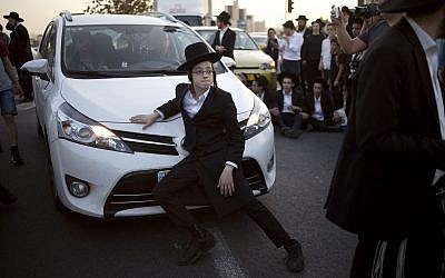 An ultra-Orthodox Jew blocks a car from crossing a main junction during a demonstration in Jerusalem against the conscription of members of the ultra-Orthodox community to the IDF on October 19, 2017. (AP Photo/Ariel Schalit)
