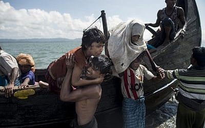Bangladeshi men help Rohingya Muslim refugees to disembark from a boat on the Bangladeshi shoreline of the Naf river after crossing the border from Myanmar in Teknaf on September 30, 2017. (AFP PHOTO / FRED DUFOUR)