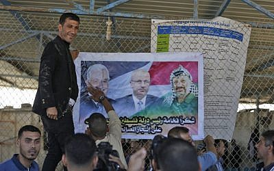 Palestinian men put up a poster displaying Palestinian leader Mahmoud Abbas (L), prime minister Rami Hamdallah and late leader Yasser Arafat, at the northern entrance of the Gaza Strip just after the Israeli-controlled Erez crossing, on November 1, 2017 in Beit Hanoun. (MAHMUD HAMS / AFP)