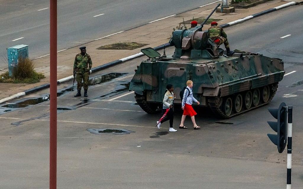 Young women walk past an armoured personnel carrier that stations by an intersection as Zimbabwean soldiers regulate traffic in Harare on November 15, 2017. (AFP PHOTO )
