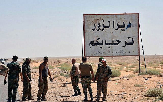 This file photo released Sept. 3, 2017, by the Syrian official news agency SANA, shows Syrian troops and pro-government gunmen standing next to a sign in Arabic which reads, "Deir el-Zour welcomes you," in the eastern city of Deir el-Zour, Syria. (SANA via AP, File) This file photo released Sept. 3, 2017, by the Syrian official news agency SANA, shows Syrian troops and pro-government gunmen standing next to a sign in Arabic which reads, "Deir el-Zour welcomes you," in the eastern city of Deir el-Zour, Syria. (SANA via AP, File)