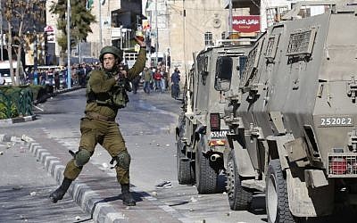 Illustrative. An Israeli soldier throws a stun grenade toward Palestinian rioters during clashes in the West Bank city of Hebron on December 8, 2017. (Hazem Bader/AFP)
