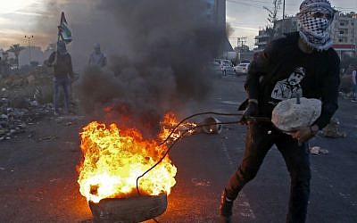 A Palestinian protester pulls a burning tire during clashes with Israeli security forces near an Israeli checkpoint in the West Bank city of Ramallah on December 9, 2017, following the US president's recognition of Jerusalem as Israel's capital. (AFP/Abbas Momani)