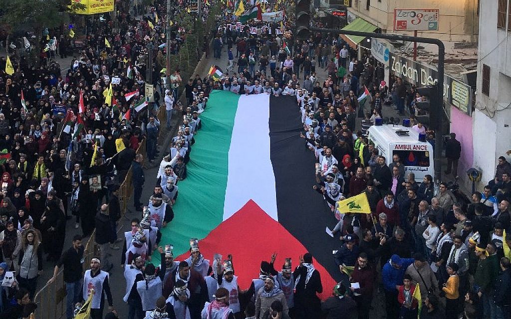 A picture taken on December 11, 2017 shows demonstrators marching with a giant Palestinian flag as they wave flags of the Hezbollah terror group in a street in the Lebanese capital Beirut, protesting against the US president's recognition of Jerusalem as Israel's capital. (AFP Photo/Joseph Eid)