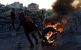 A Palestinian demonstrator moves a burning tire during clashes with Israeli forces near an Israeli checkpoint in the West Bank city of Ramallah on December 16, 2017l.  (AFP PHOTO / ABBAS MOMANI)