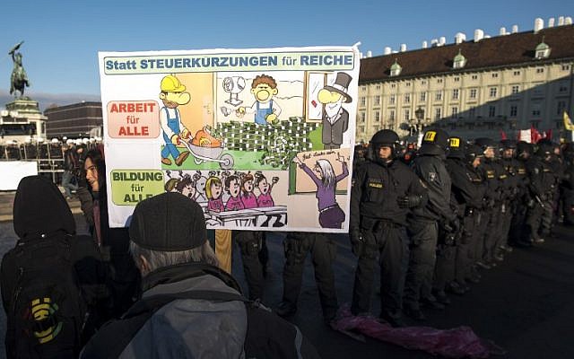 A demonstrator with a banner reading "Instead of tax cuts for the rich, work for all !" stands next to riot police during a protest against the new Austrian government near the presidential palace during the inauguration of the new Austrian government in Vienna, Austria, on December 18, 2017. ( AFP PHOTO / JOE KLAMAR)