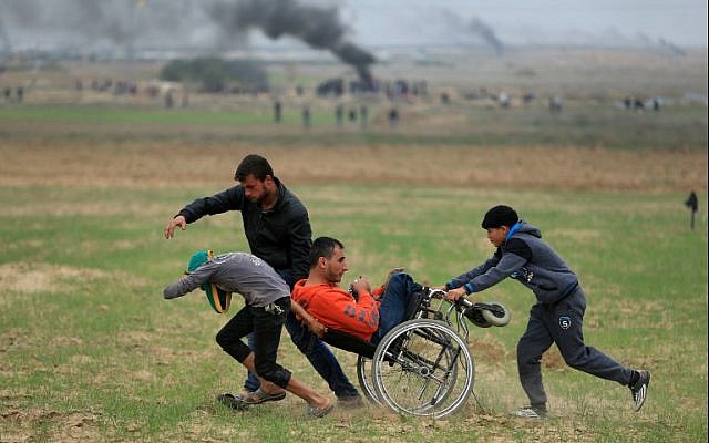 Palestinians assist a demonstrator in a wheelchair during clashes with Israeli security forces near the border fence east of Gaza City on December 22, 2017. (AFP Photo/Mohammed Abed) Palestinians assist a demonstrator in a wheelchair during clashes with Israeli security forces near the border fence east of Gaza City on December 22, 2017. (AFP Photo/Mohammed Abed)