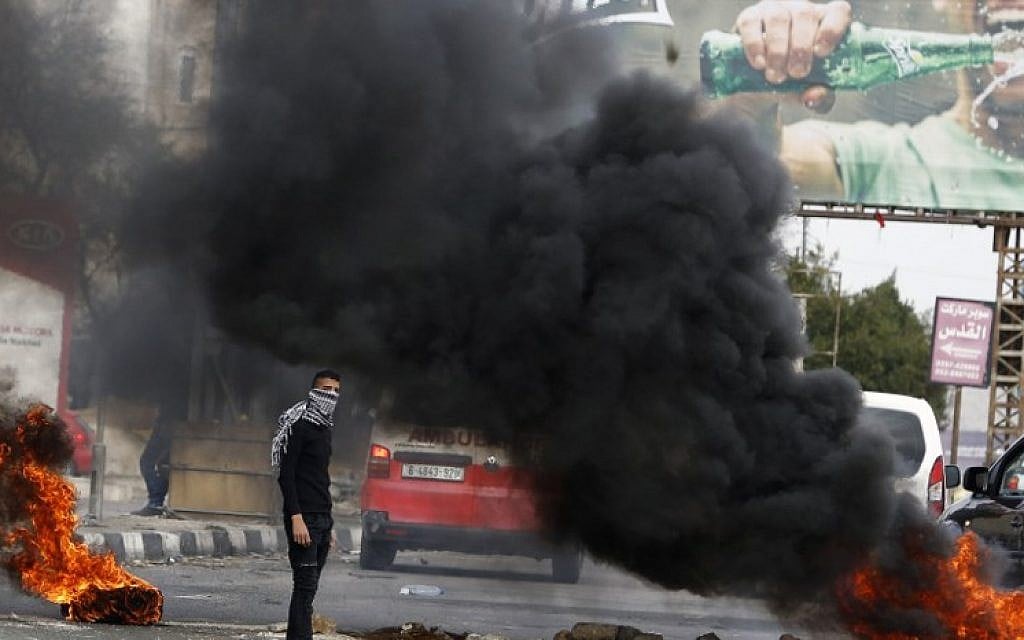 A Palestinian protester stands near flaming tires during clashes with Israeli soldiers near the Huwara checkpoint, south of Nablus in the West Bank on December 27, 2017. (AFP /JAAFAR ASHTIYEH) A Palestinian protester stands near flaming tires during clashes with Israeli soldiers near the Huwara checkpoint, south of Nablus in the West Bank on December 27, 2017. (AFP /JAAFAR ASHTIYEH)