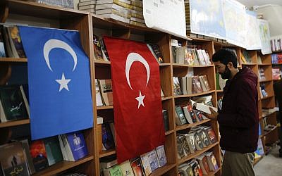 In this photo taken Thursday, Dec. 14, 2017, a man reads a book in a bookstore where flags which represents Turkey and 'East Turkistan,' the name Uighurs who oppose Chinese rule call their homeland, are hung in Istanbul's Zeytinburnu neighborhood. (AP Photo/Emrah Gurel)